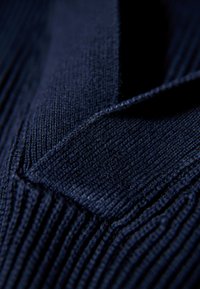 Tessuto a maglia di colore blu navy con un motivo testurizzato caratterizzato da righe verticali. Il materiale appare morbido ed elastico nei punti di cucitura.