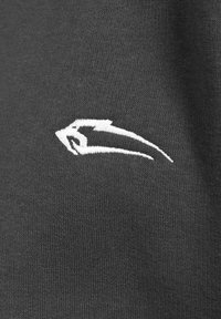 Ciemnoszara tkanina zbliżenie na białe haftowane logo, charakteryzujące się eleganckimi, kanciastymi liniami oraz stylizowanym wzorem.