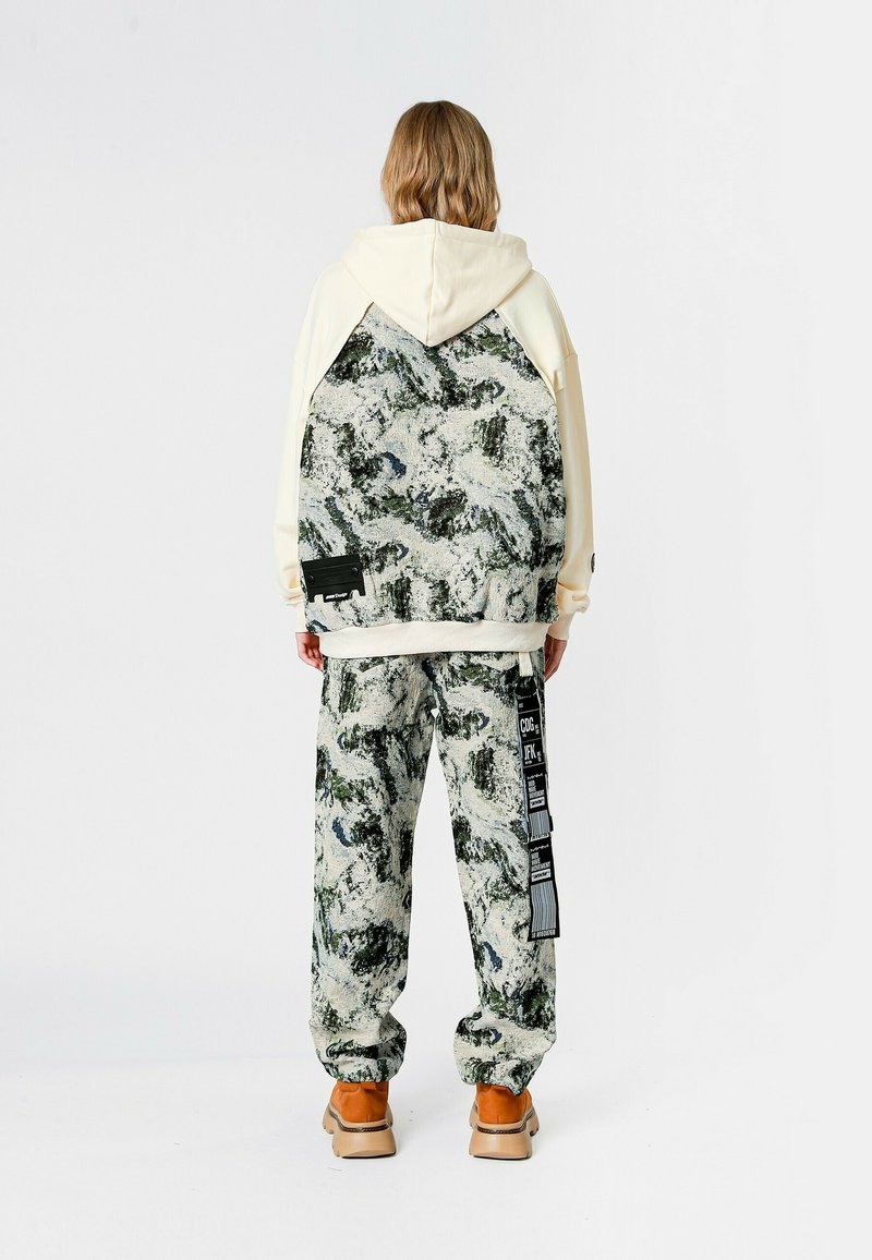 Sudadera con capucha en color crema con un patrón texturizado en verde y blanco en la parte trasera, combinada con pantalones a juego con el mismo patrón y zapatos color marrón claro.