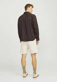 Dunkelbraunes Langarmhemd mit Knöpfen, beige Shorts und hellen Sneakers. Baumwollstoff, strukturierte Gestaltung, minimale Details.