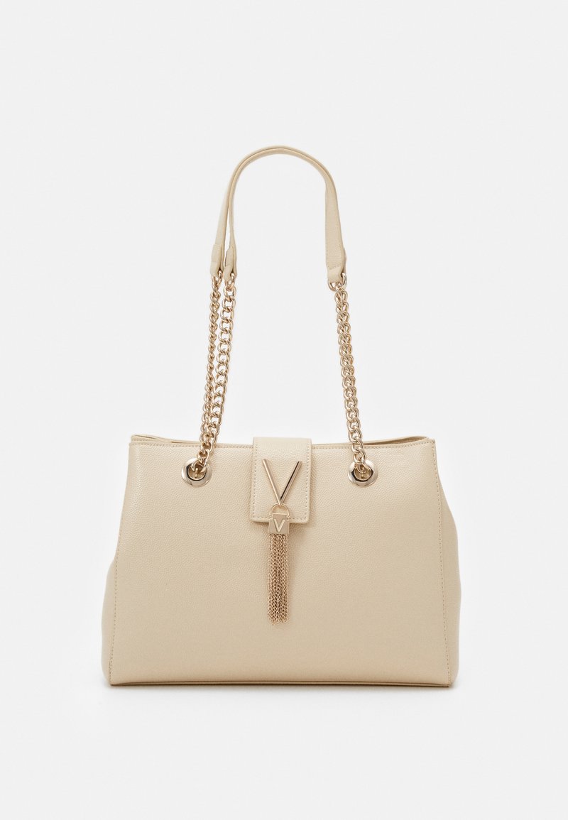 Beige Tote Bag aus Kunstleder mit goldenen Kettenriemen, rechteckiger Form, V-Logo an der Vorderseite und dekorativem Quastendetail. Glatte Textur.