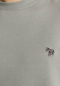 Sudadera gris con cuello redondo y textura acanalada, con un logo de cebra bordado en multicolor en el lado izquierdo del pecho.