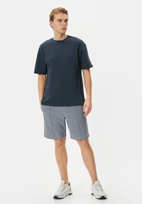 Kaos berkerah lengan pendek berwarna biru navy dipadukan dengan celana pendek bermotif abu-abu, dengan potongan santai. Alas kaki berupa sepatu sneaker putih dengan aksen hitam.
