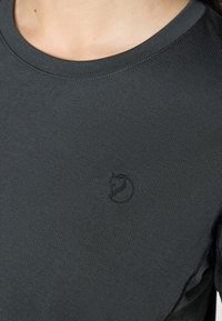 Tmavo sivá polokošeľa s krátkym rukávom vyrobená z texturovanej látky, s malým vyšitým logom líšky na ľavej strane hrude.