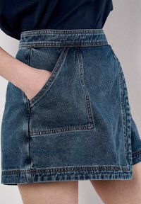 Dunkelblaue Jeansrock mit einer vorderen Tasche und sichtbaren Nähten. Gerade Silhouette mit einem Saum über dem Knie.