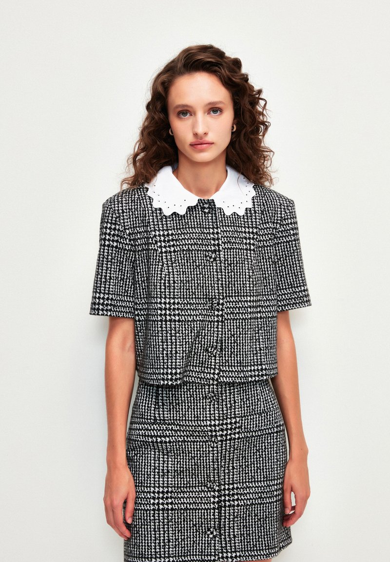 Zwart-wit gestreepte cropped jack met korte mouwen, gestructureerde stof, en een witte, scalloped kraag shirt eronder.