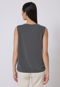 Top gris sin mangas con escote redondo, hecho de una tela suave, con un ajuste relajado y una textura sutil. La vista trasera muestra una longitud uniforme.