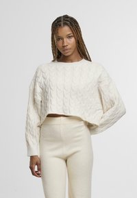 White cable-knit cropped sweater with oversized sleeves, paired with matching cream fitted pants. Textured knit and ribbed cuffs.