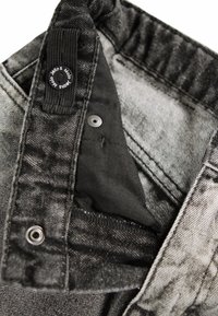 Black denim jeans with a soft inner lining, featuring a metal snap button and a woven label at the waistband. Distressed texture detail visible.
