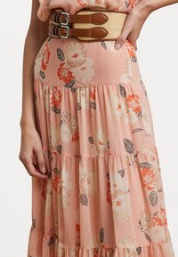 Blomstrete lagdelt kjole i myk ferskenfarge med oransje og beige blomster. Kombinert med et bredt vevd belte med brune lærdetaljer og doble spenner.