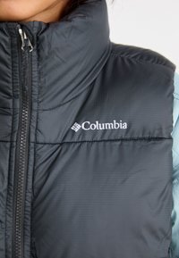 Must must vest kõrge kraega, lukuga sulgemine ja Columbia logo. Omab peent triibutekstiili ning puhvkujundust soojuse tagamiseks.