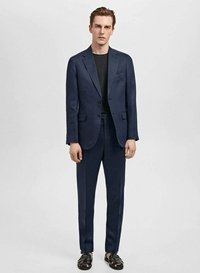Costume bleu marine avec une veste structurée et un pantalon ajusté, associé à un haut noir et des chaussures. Tissu lisse et détails minimaux.