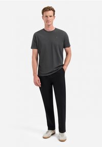 Grijze katoenen T-shirt met een ronde hals, gecombineerd met zwarte broek en witte sneakers, staand op een effen achtergrond.