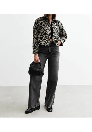 Persona con chaqueta con estampado de leopardo, top corto negro, vaqueros oscuros de pierna ancha, mocasines negros, sosteniendo un bolso pequeño negro.