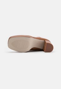 Chaussure en cuir brun avec un bout arrondi, un talon carré modéré et une semelle en caoutchouc texturé comportant des rainures horizontales pour une meilleure adhérence.
