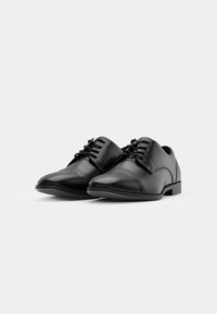 Zapatos de vestir de cuero negro con punta redondeada, textura lisa, cierre con cordones y diseño minimalista. Suela de goma para tracción.