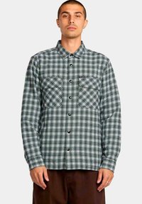 Camisa de cuadros de manga larga en verde y blanco, con dos bolsillos en el pecho y botones negros. Tela de algodón con un acabado texturado.