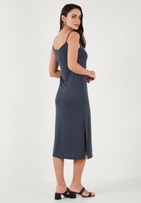 Merenneito sininen, hihaton midi-mekko, jossa on sivuhaalari, istuva muotoilu, sileä rakenne ja minimalistinen tyyli, yhdistettynä mustiin korkokenkiin.