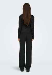 Maglietta nera a maniche lunghe con finitura testurizzata e taglio aderente, abbinata a pantaloni neri larghi. L'outfit presenta un design elegante e accenti minimali.