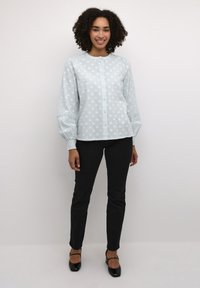 Lichtblauwe blouse met textuur en stippen, met knopen aan de voorkant, ronde halslijn en gathered mouwen. Gepaarde met zwarte slim-fit broek en hakken.