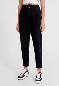 Svarta byxor med en avslappnad passform, utrustade med resår i midjan, uppvikta benslut och sidofickor, i kombination med svartvitt sneakers.