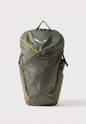 Sac à dos vert olive avec fermeture éclair diagonale, poches latérales marron, accents jaunes et poignée supérieure, debout sur un fond blanc uni.