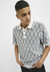 Polo krekls baltā un tumši zila zivju kaula rakstā, ar adītu tekstūru, kontrastējošu apkakli un trim pogām pie kakla.