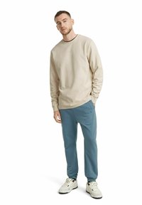 Beige sweatshirt with crew neckline paired with light blue joggers. Soft fabric, relaxed fit, and side pockets. White sneakers complete the look.