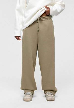 Beige, losvallende sweatpants met een trekkoord in de taille, zacht materiaal en een wijdbenig ontwerp. Gecombineerd met een witte sweatshirt met lange mouwen.