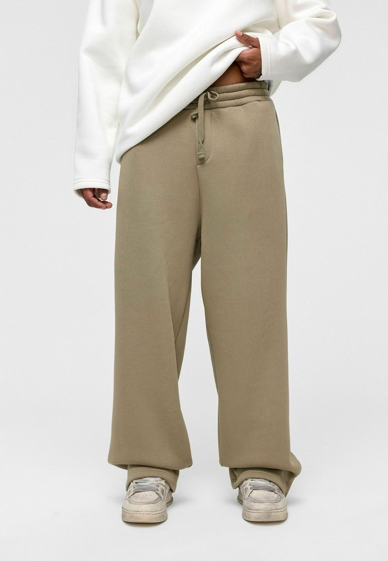 Beige, losvallende sweatpants met een trekkoord in de taille, zacht materiaal en een wijdbenig ontwerp. Gecombineerd met een witte sweatshirt met lange mouwen.