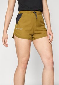 Olive green shorts with a drawstring waist, black mesh side pockets, and a logo detail. The fabric is smooth and lightweight.