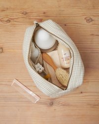 Beige sminkepung med rutemønster og glidelås, som inneholder flasker, en trebørste, en kam og små hygieneartikler. Strukturert innside.