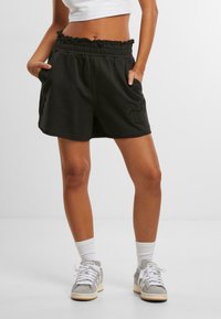 Sorte bomullsshorts med volangliv, sidelommer og brodert mønster foran. Kombinert med grå joggesko og hvite sokker.