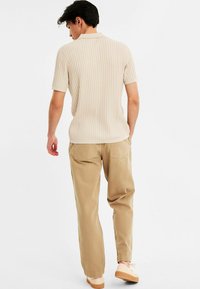 Beige knitted polo shirt with short sleeves, paired with light tan chinos and beige slip-on shoes, viewed from the back.