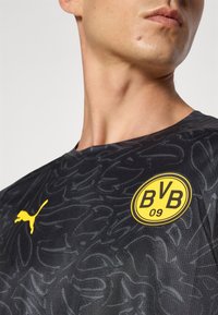 Sort sportsjersey med et tekstureret mønster, rund halsudskæring, gul Puma-logo og cirkulært Borussia Dortmund-mærke med "BVB 09."