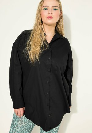 Schwarzes oversized Hemd mit Knopfleiste, langen Ärmeln, weichem Stoff und abgerundetem Saum, kombiniert mit hellblauen Leggings im Leopardenmuster.