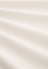 Struktureret hvidt stof med et subtilt gittermønster, glat overflade og blødt fald, velegnet til forskellige tekstilapplikationer.