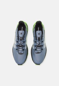 Chaussures de course en trail bleu avec des accents noirs et des détails vert vif, présentant une tige texturée, un système de laçage sécurisé et une semelle extérieure durable.