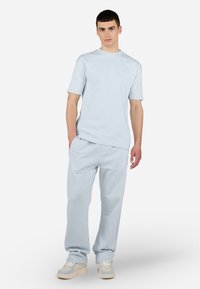 Lichtblauw katoenen T-shirt en bijpassende trainingsbroek, met een relaxte pasvorm. T-shirt heeft korte mouwen en minimale branding op de borst. Sneakers zijn beige.