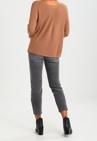 Hnědý pletený svetr se širokým výstřihem, kombinovaný se šedými džínami a černými kotníkovými botami. Svetr má volný střih a žebrovanou texturu.