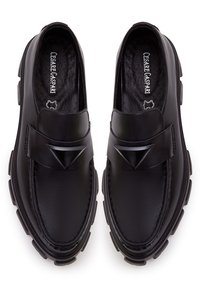 Mocassins en cuir noir avec des semelles épaisses, décorations noires triangulaires sur les sangles et marque "Cesare Gaspari" à l'intérieur.