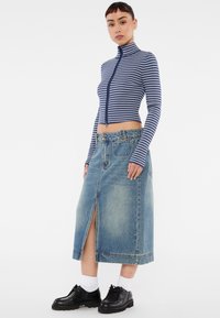 Marineblauwe en witte gestreepte lange mouwen met een rits en hoge kraag, gecombineerd met een lichtblauwe denimrok met een split aan de voorkant. Zwarte schoenen.