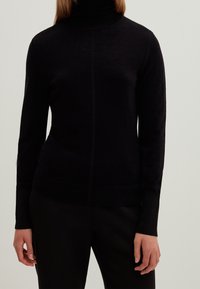 Mustakotoinen poolopaita pehmeästä materiaalista, jossa on pitkät hihat, kapea istuvuus ja sauma etuosassa.