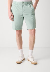 Lys grønne shorts lavet af glat stof, med elastisk talje, sidelommer og lige snit, parret med hvide sneakers.