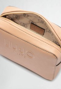 Trousse de maquillage texturée couleur pêche avec fermeture éclair dorée. L'intérieur présente un motif logo et une étiquette marron. Logo embossé sur le devant.