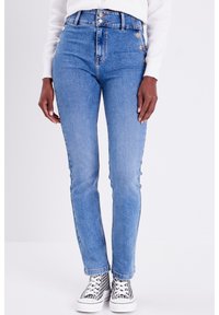 Jean bleu taille haute avec un design à cinq boutons, poches avant et coupe skinny. Associé à des baskets à motifs noir et blanc.