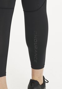 Schwarze Performance-Leggings mit einer eleganten, glatten Textur verfügen über ein auffälliges "ENDURANCE"-Logo in Grau an der Seite. Entwickelt für aktive Freizeitkleidung.
