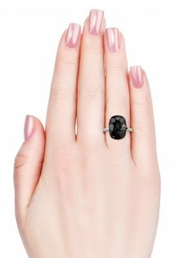 Anello con pietra ovale nera incastonata in una fascia d'argento, esposto su una mano con smalto rosa, che mette in risalto i lati della gemma e la finitura liscia del metallo.