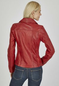 Rode leren jas met een aansluitend ontwerp, notch-kraag en zichtbare stikseldetails. Draagt met donkerblauwe denim jeans.