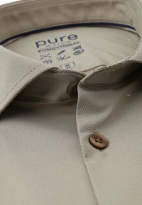 Beige overhemd met kraag, gemaakt van gestructureerde stof, met twee bruine knopen en een label aan de binnenkant met wasymbolen en het merk "pure".